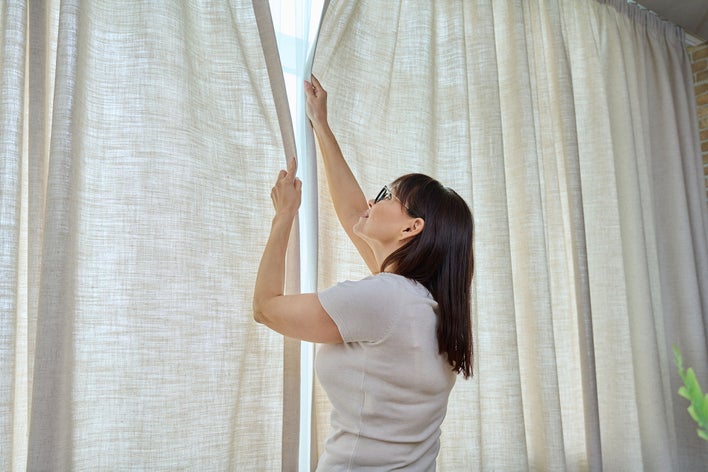 Woman hanging curtains in her home as a way to reduce noise pollution.