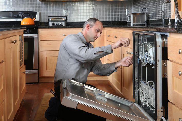 A man installing a new dishwasher as part of a DIY home remodel project.