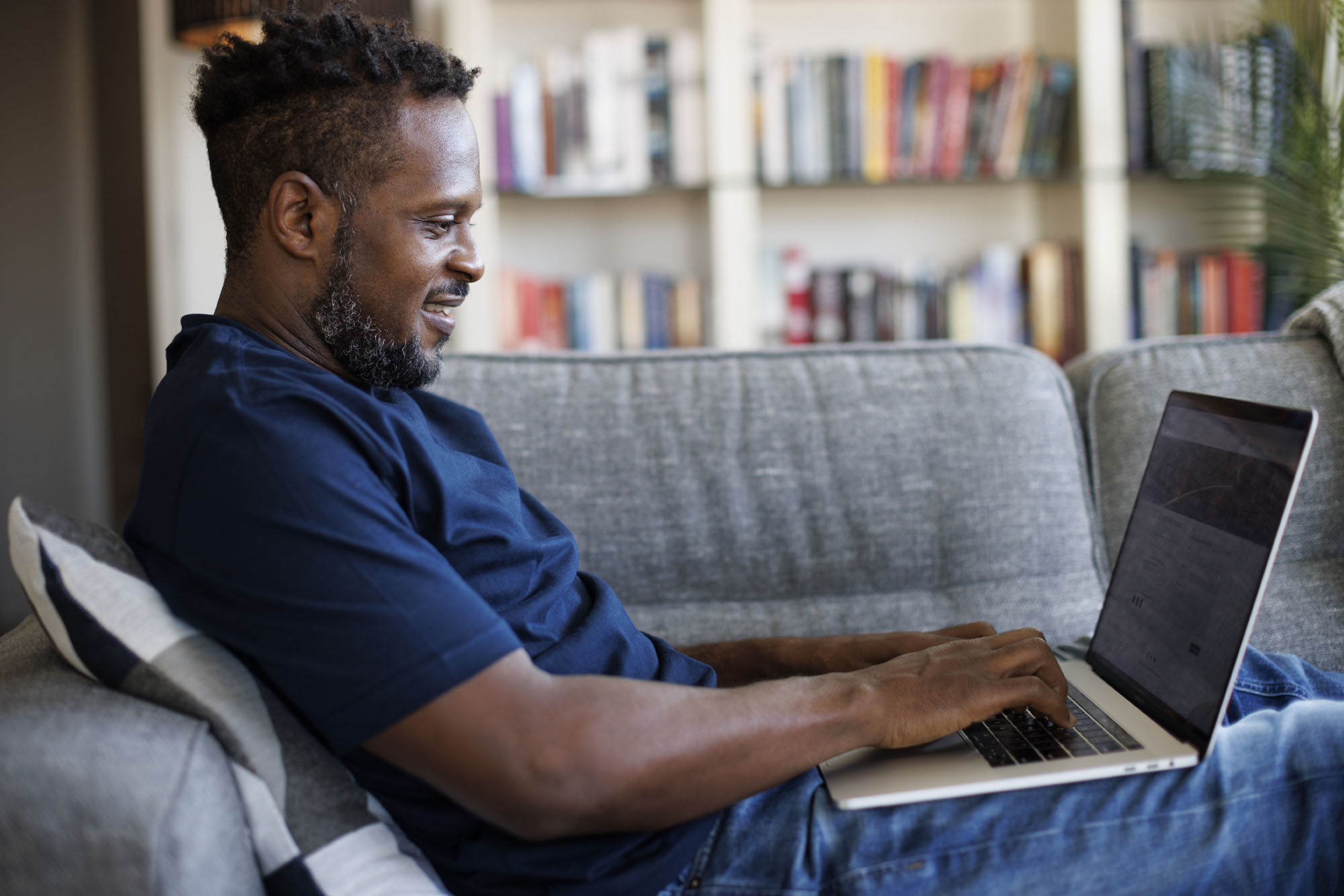 Man happily updating his address online while sitting on a couch as part of his new home checklist.