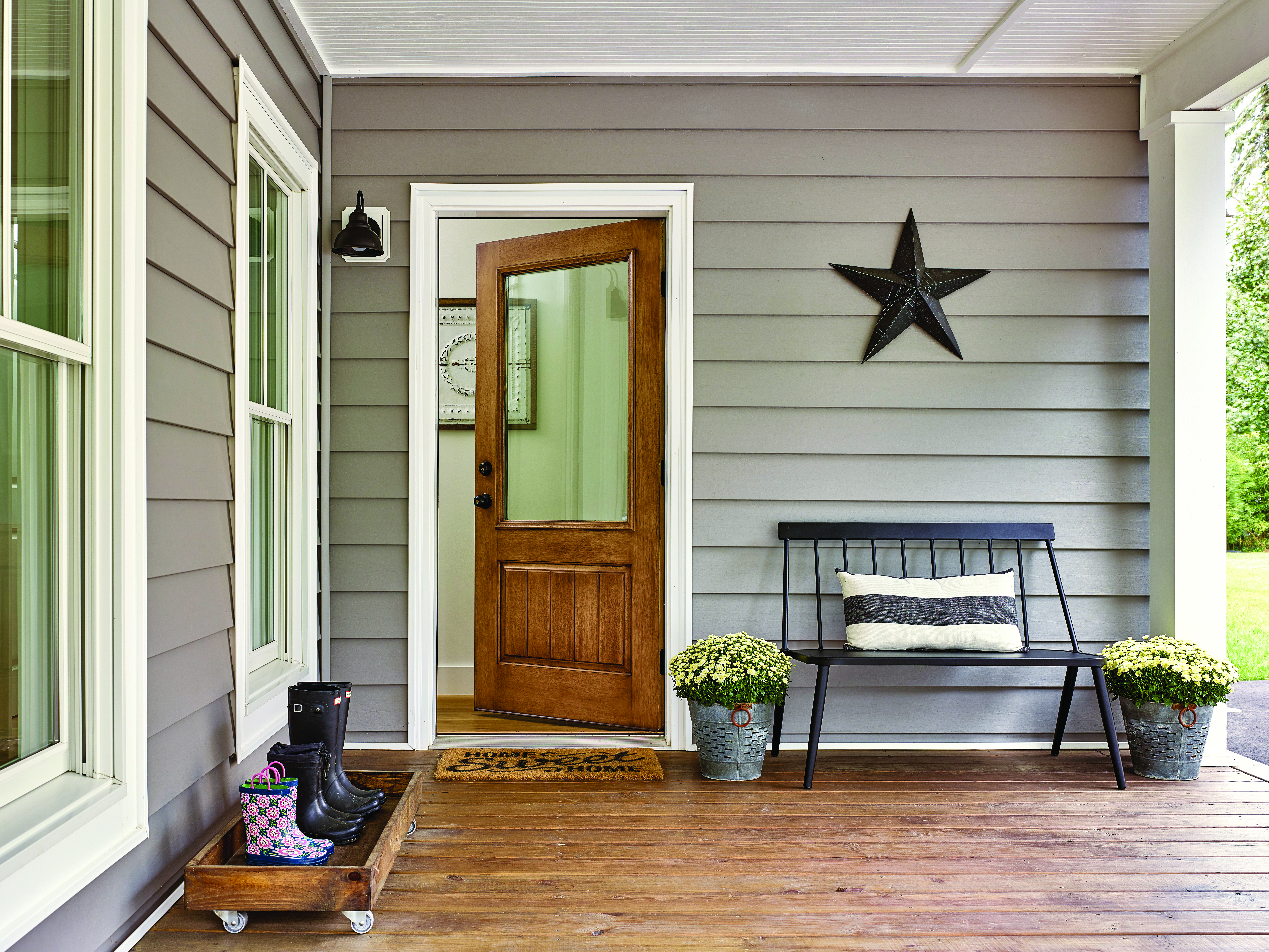 Mahogany finish front door installed on a gray-colored home in front of a 'home sweet home' mat.