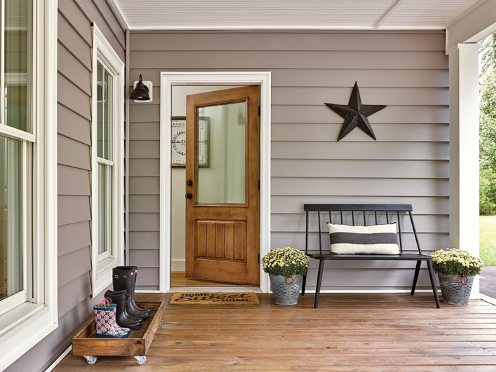 Mahogany finish front door installed on a gray-colored home in front of a 'home sweet home' mat.