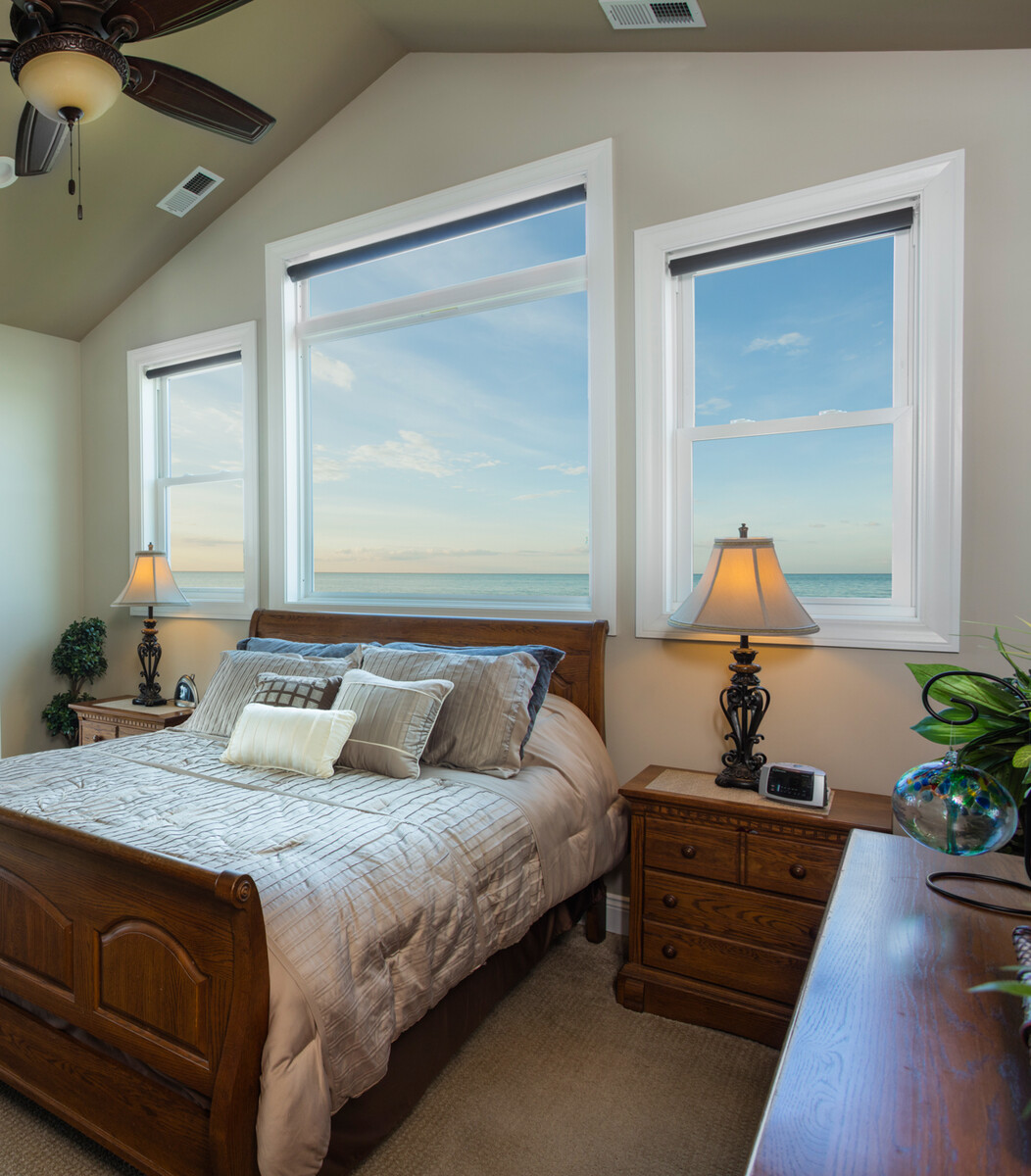sleek picture window above sleigh bed offering an oceanfront view with flanking double hung windows