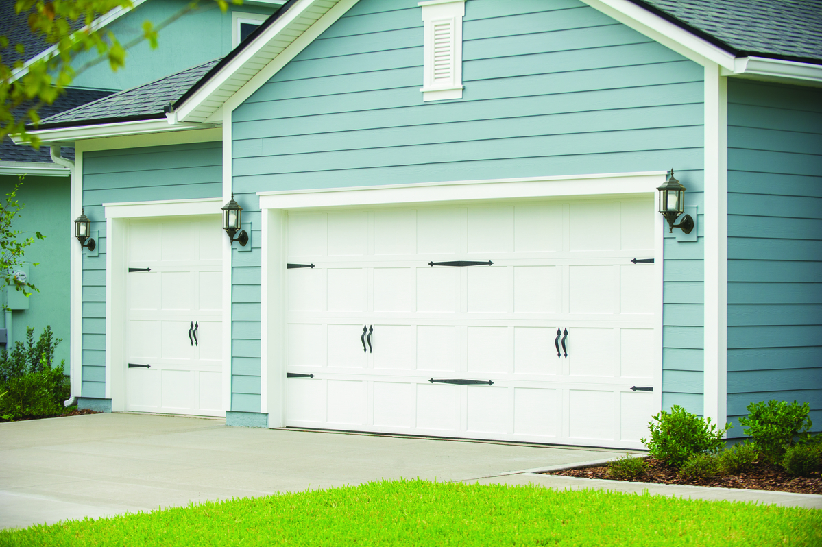 White short panel garage door with no windows and decorative hardware installed on ranch home with baby blue siding 