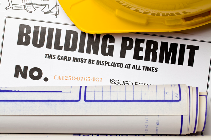 A close-up of a building permit, yellow hard hat, and blueprints for a DIY home renovation.