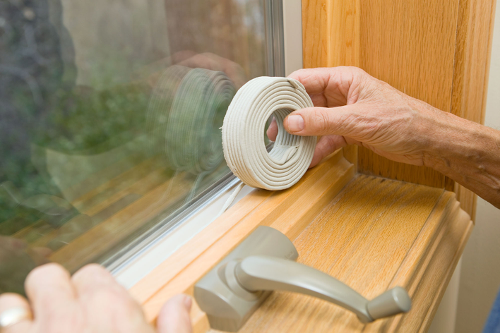 Person sealing windows with weatherstripping to prevent exterior window condensation at home.