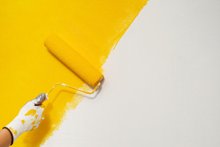 A hand painting a wall bright yellow with a roller