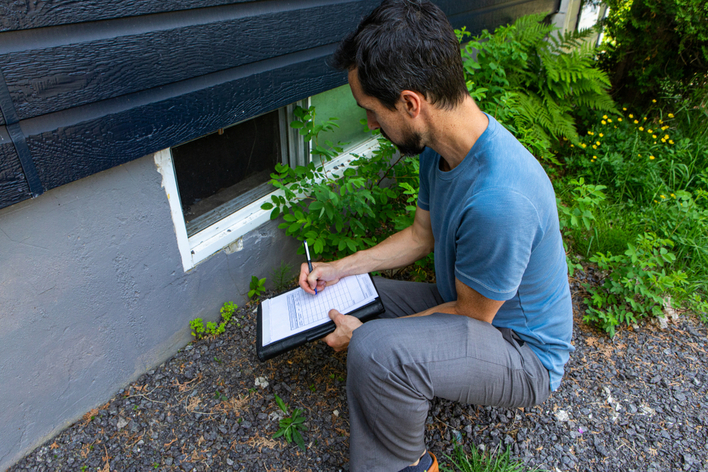 A man preparing a home for hurricane season by inspecting the home’s foundation and basement window