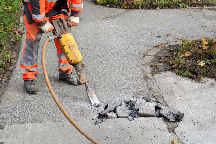 Construction worker using a jackhammer on the sidewalk in a neighborhood.