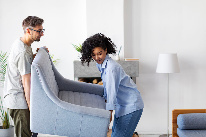 A couple lifting and adjusting a chair in their living room to prepare for a window installation at their home.