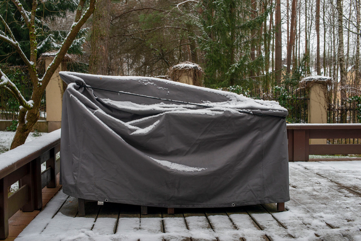 A large piece of outdoor furniture winterized with the appropriate cover and dusted with snow