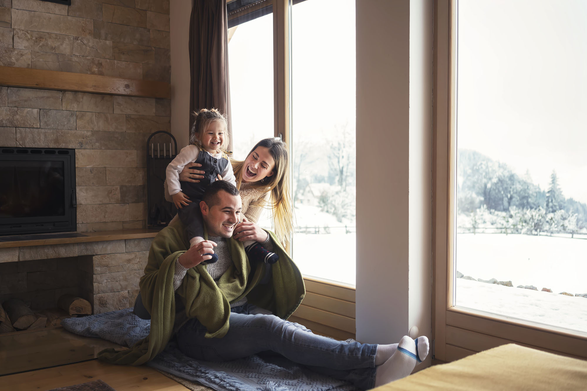 A family laughing together beside large windows overlooking a wintery landscape.
