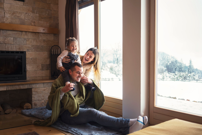 A family laughing together beside large windows overlooking a wintery landscape.