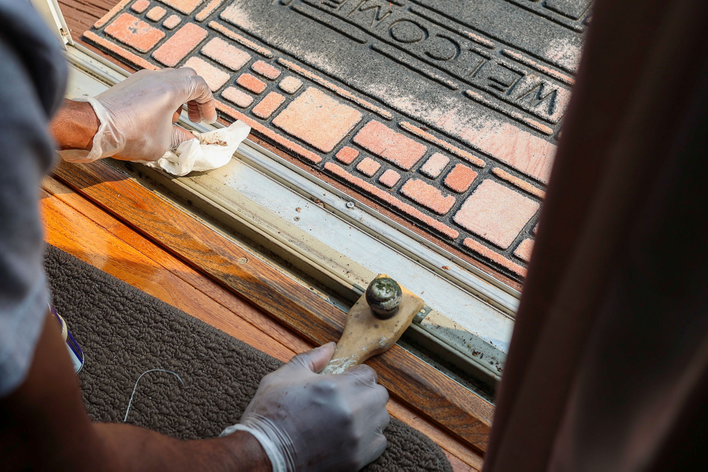 A man cleaning a patio door track to better maintain doors for the winter season.