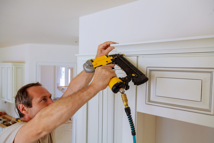 Man adding white crown molding above kitchen cabinets