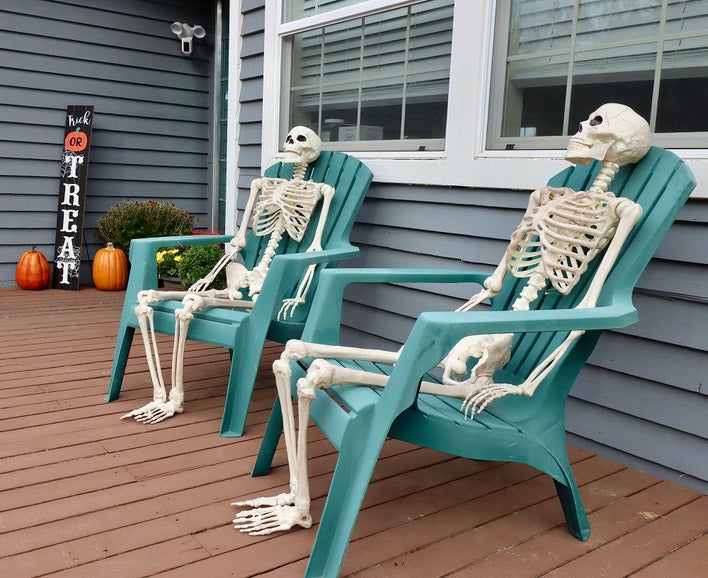 Two skeletons placed in teal lawn chairs in front of a home as Halloween decorations.