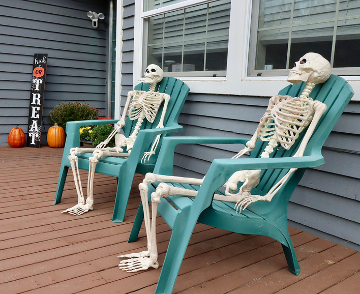 Two skeletons placed in teal lawn chairs in front of a home as Halloween decorations.