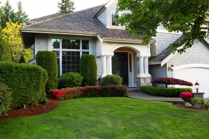 White and gray home surrounded by outdoor plants and a well-kept lawn.