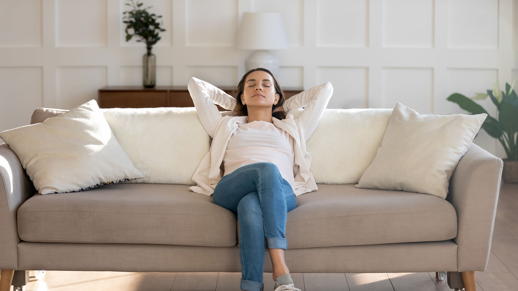 A woman resting on a couch that is exposed to natural light by nearby windows.