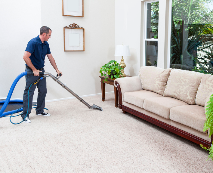 Man vacuuming the beige carpet of his old home.