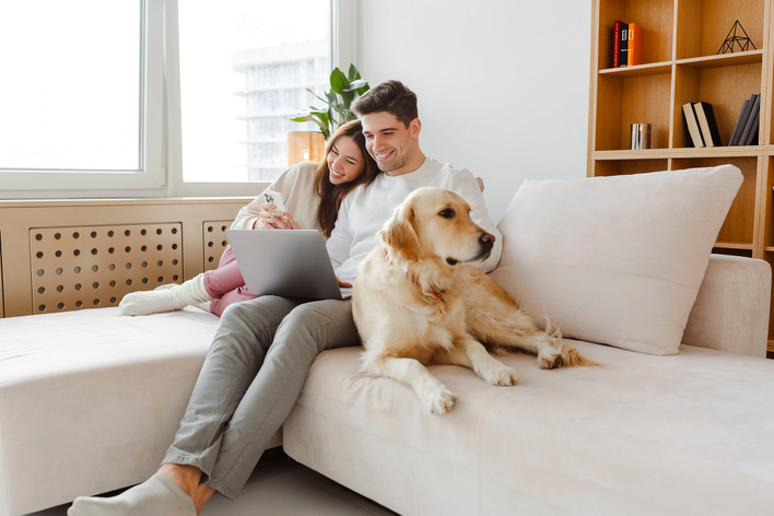 A couple sitting on a couch with their dog, researching ways to reduce carbon footprint on a laptop.