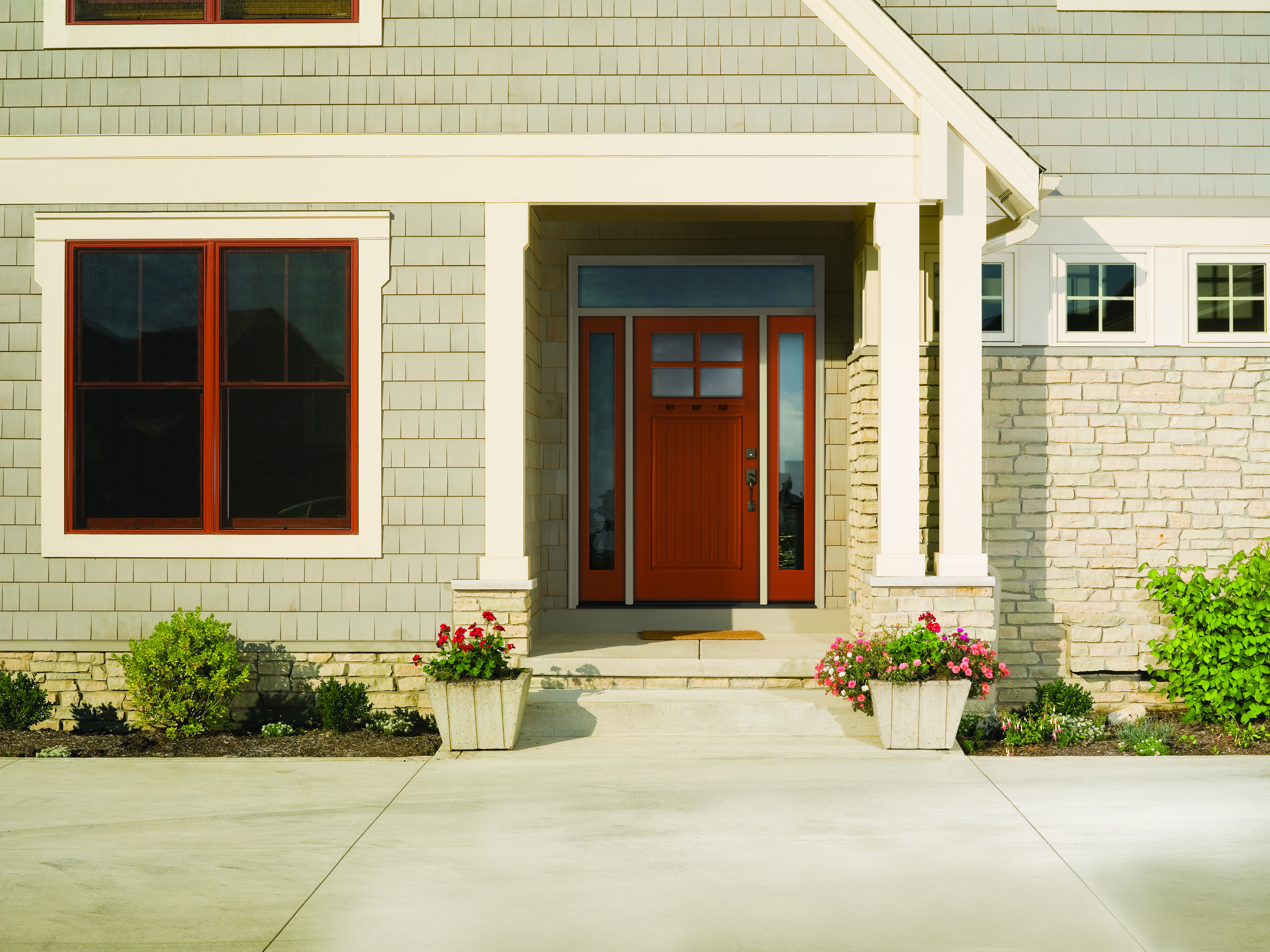 Smooth fiberglass entry door installed on a home in front of a porch with a welcome mat and potted plants.