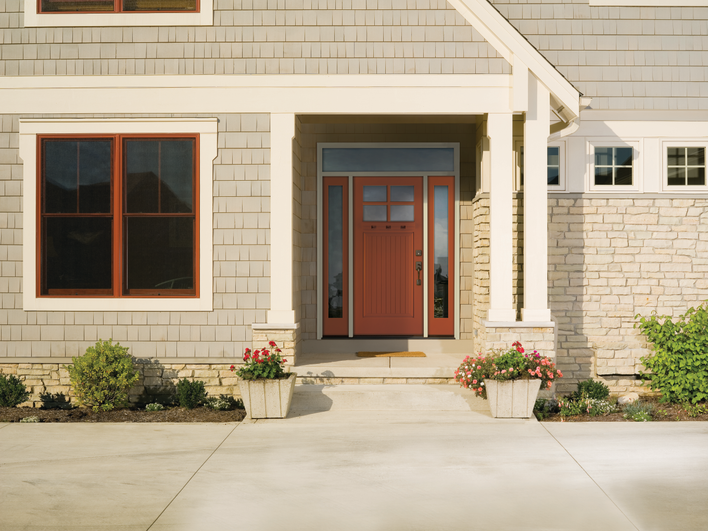 Smooth fiberglass entry door installed on a home in front of a porch with a welcome mat and potted plants.