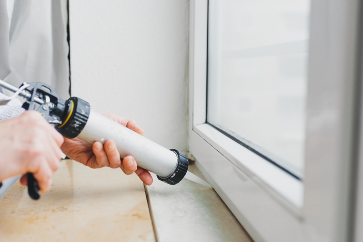 A new homeowner applying caulk around a window in their first home.