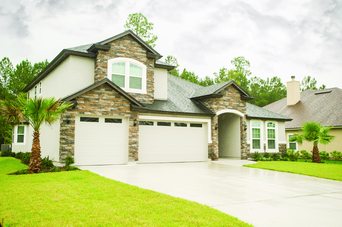 Gray long panel garage door with clear windows installed on a two-story stone home