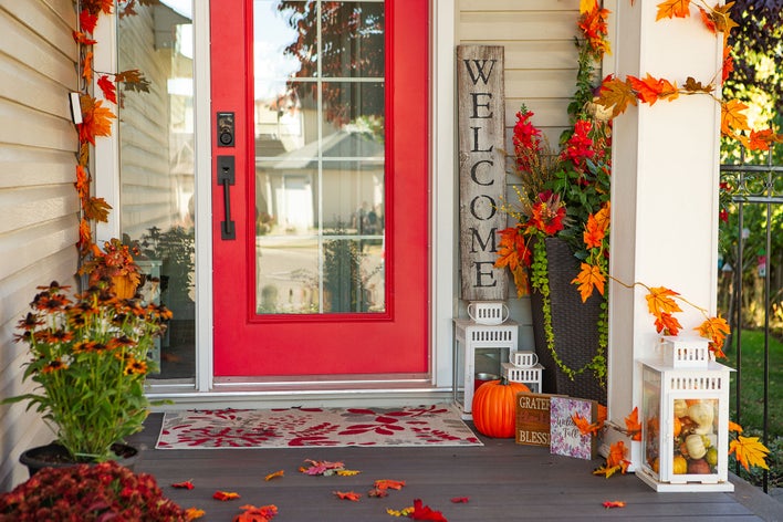 Red entry door of a home with autumn-themed decorations surrounding the front porch.