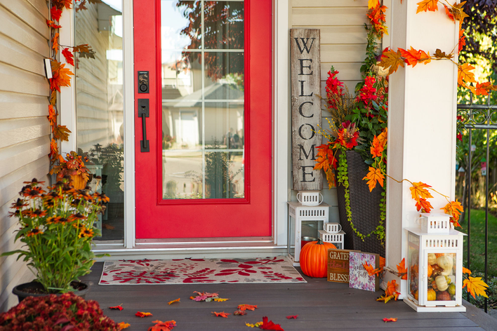 Red entry door of a home with autumn-themed decorations surrounding the front porch.