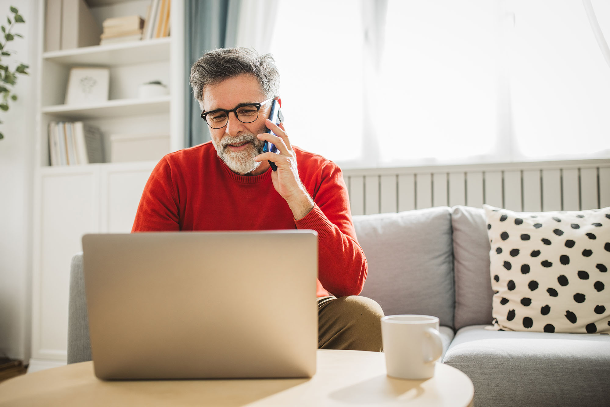 Man calling the utility companies as he reviews new home checklist on laptop while sitting on couch.
