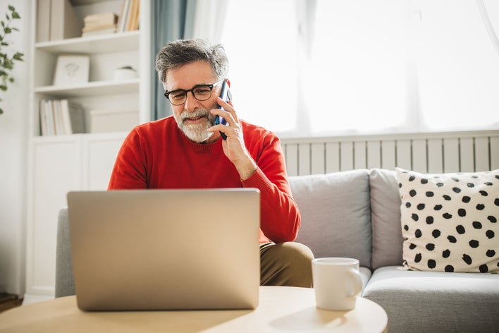 Man calling the utility companies as he reviews new home checklist on laptop while sitting on couch.