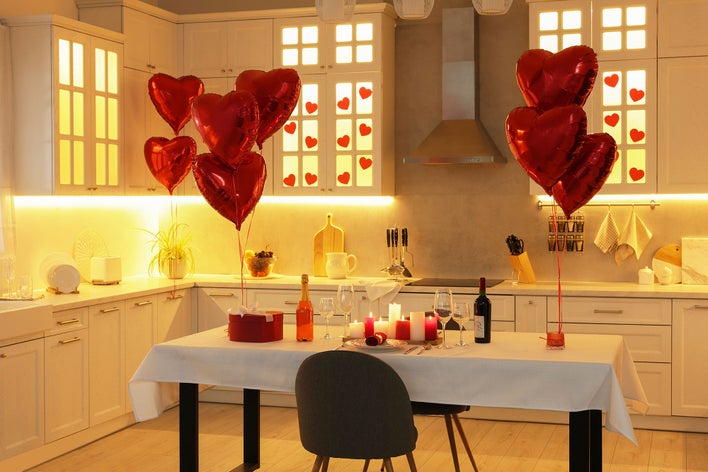 A kitchen decorated with romantic Valentine’s Day elements: heart-shaped balloons, redand white candles, warm lights, and a red gift box.