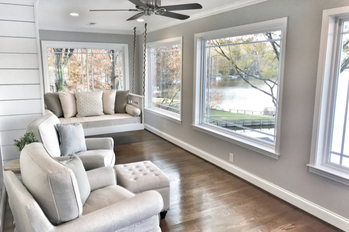 Neutral-colored sitting room with wood floors and large picture windows overlooking a lake