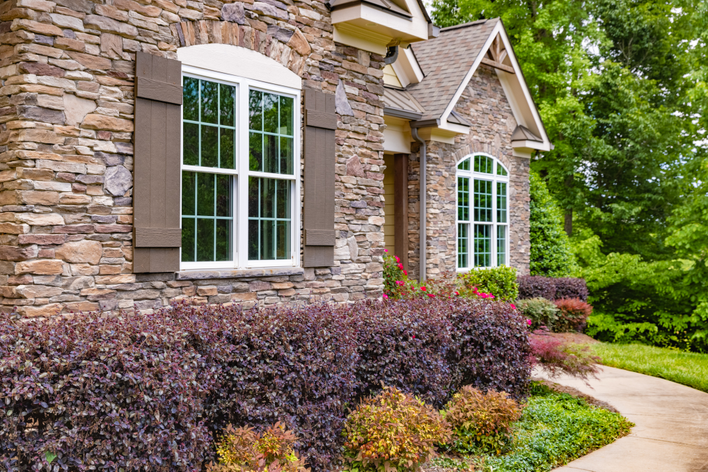 Brick home insulated with energy-efficient windows surrounded by shrubbery.