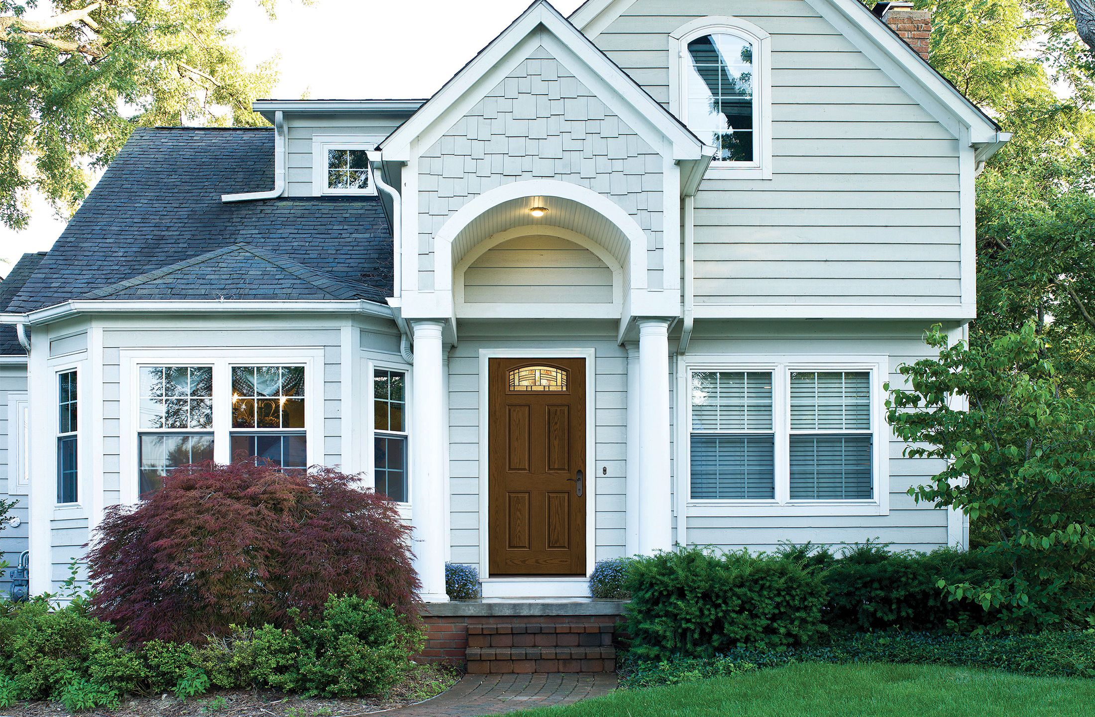 A Barley colored Fiber-Classic® Fiberglass Entry Door on a lighter-colored 2- story house with a dark roof
