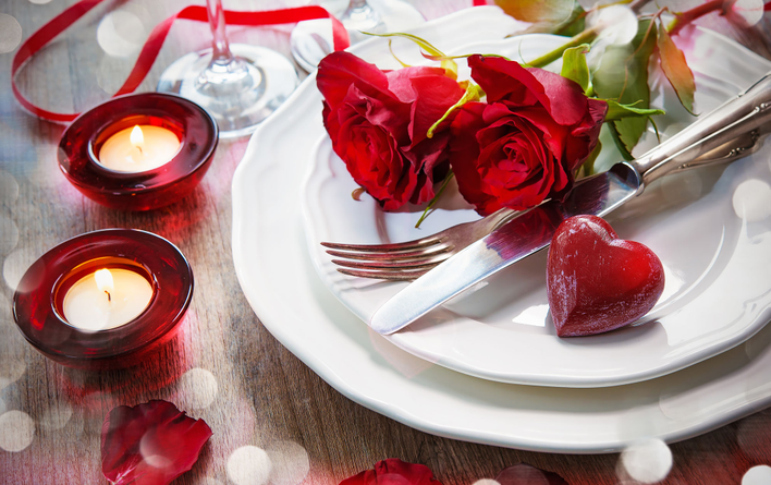 A romantic Valentine’s Day place setting, complete with red roses and votive candles.