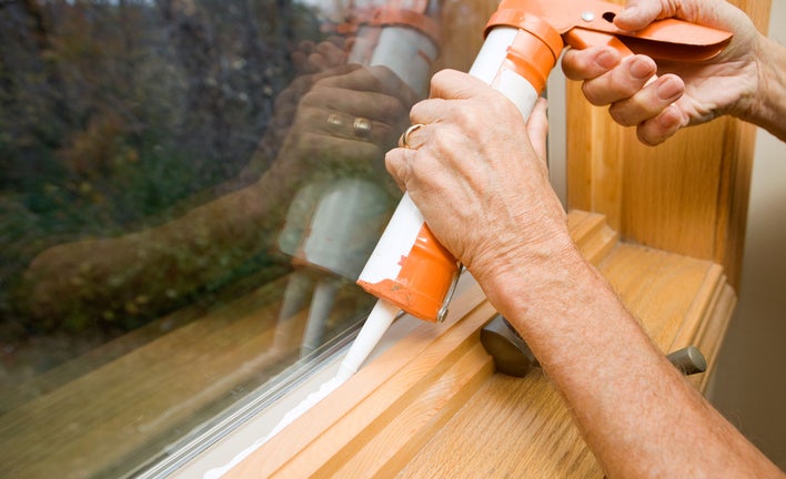 Person using caulk to seal windows in the home to prevent air drafts or leaks to help reduce the electric bull during winter.