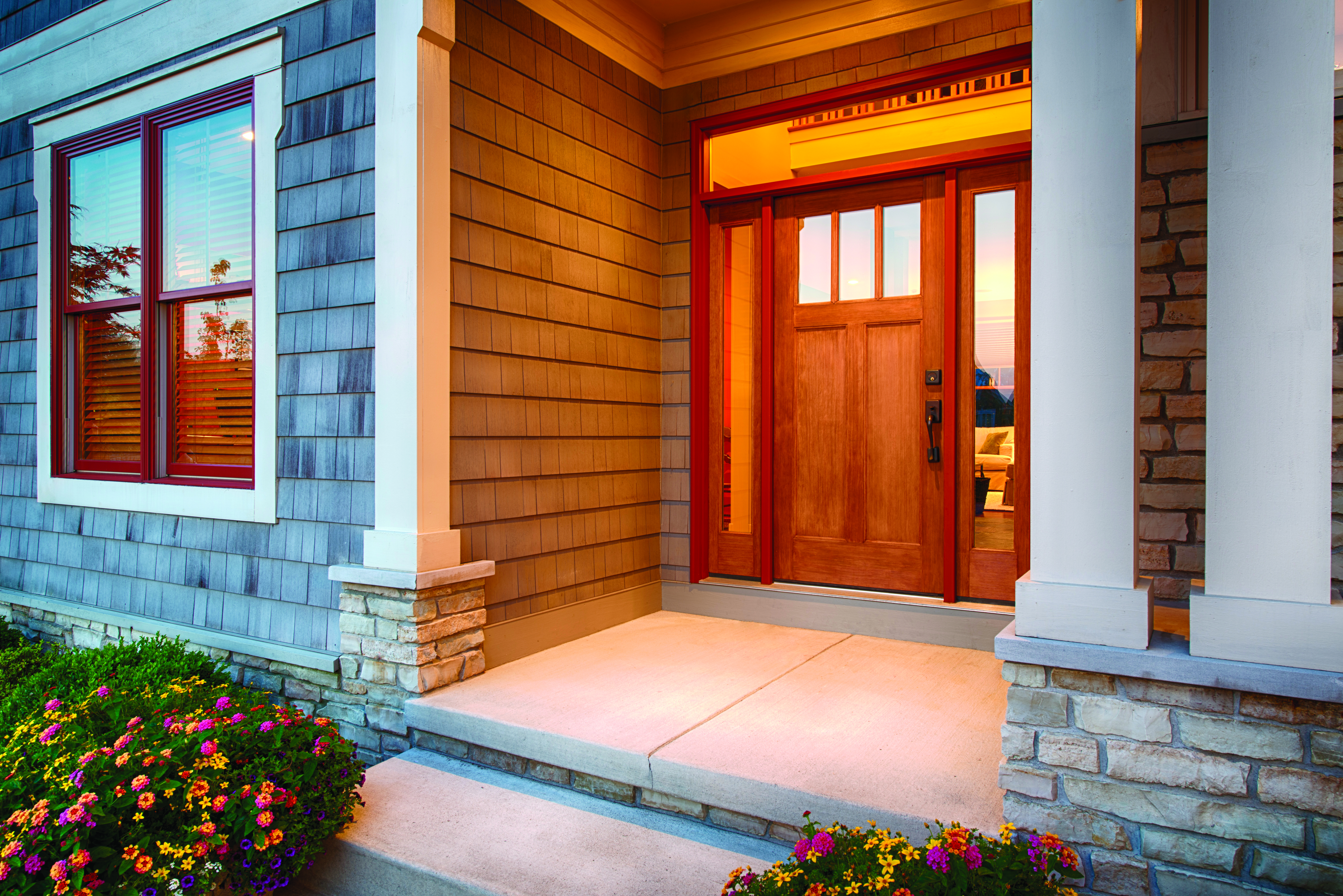 The front porch of a house with a woodgrain fiberglass door, gray siding, and white<br>columns.