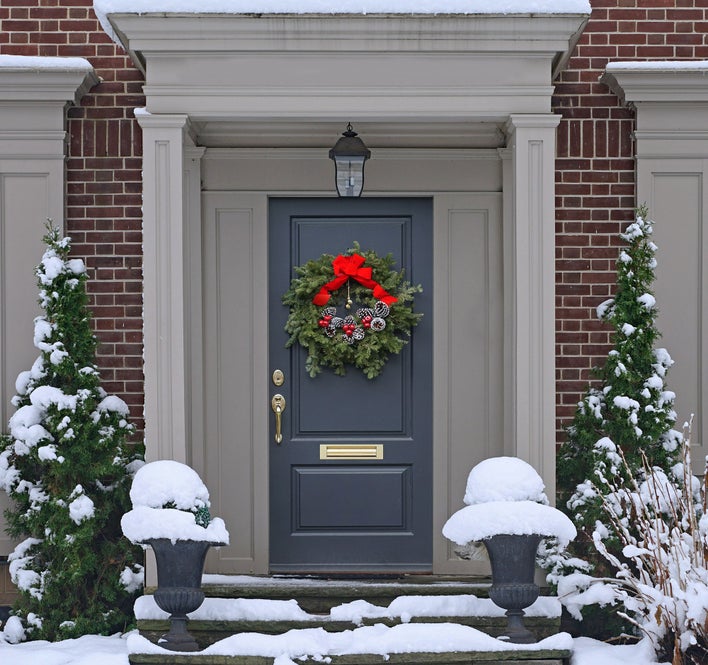 A snow-covered entryway brightened by a Christmas wreath with pinecones and red berries hung on the door.