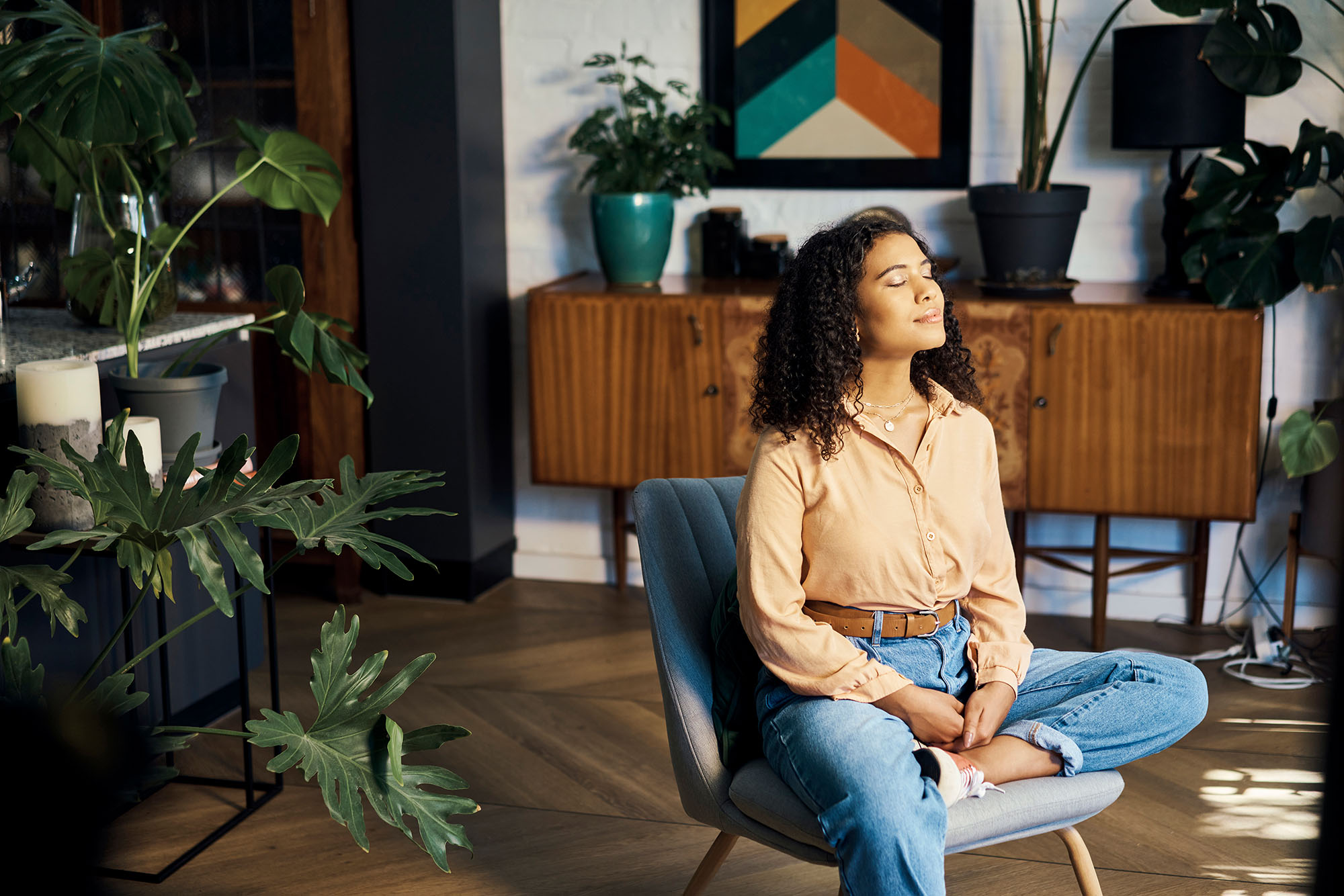 Woman enjoying reduced noise pollution at home as she sits in a chair in the middle of a room surrounded by plants.