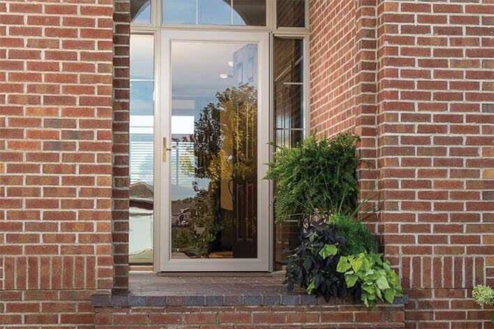A full view storm door protects the interior of a brick house while the main entry door is open to let in light