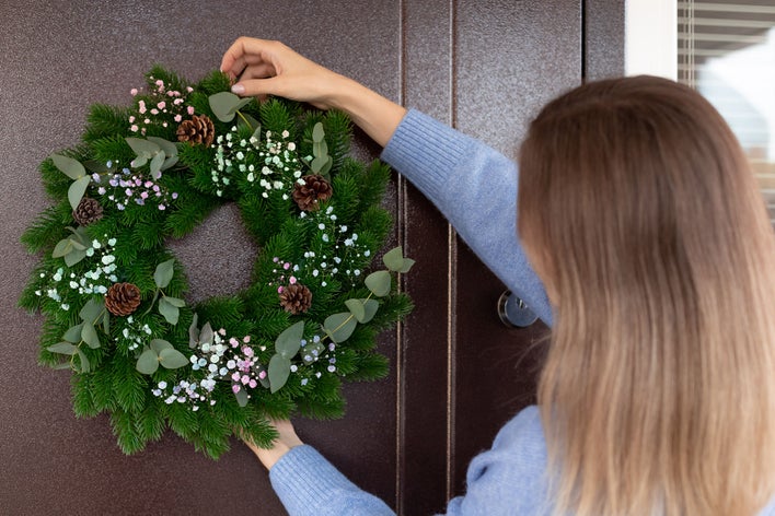 A woman deciding the best way to hang a wreath as she decorates for the holidays.