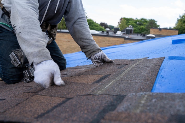 Gloved hands installing a row of shingles on a roof.