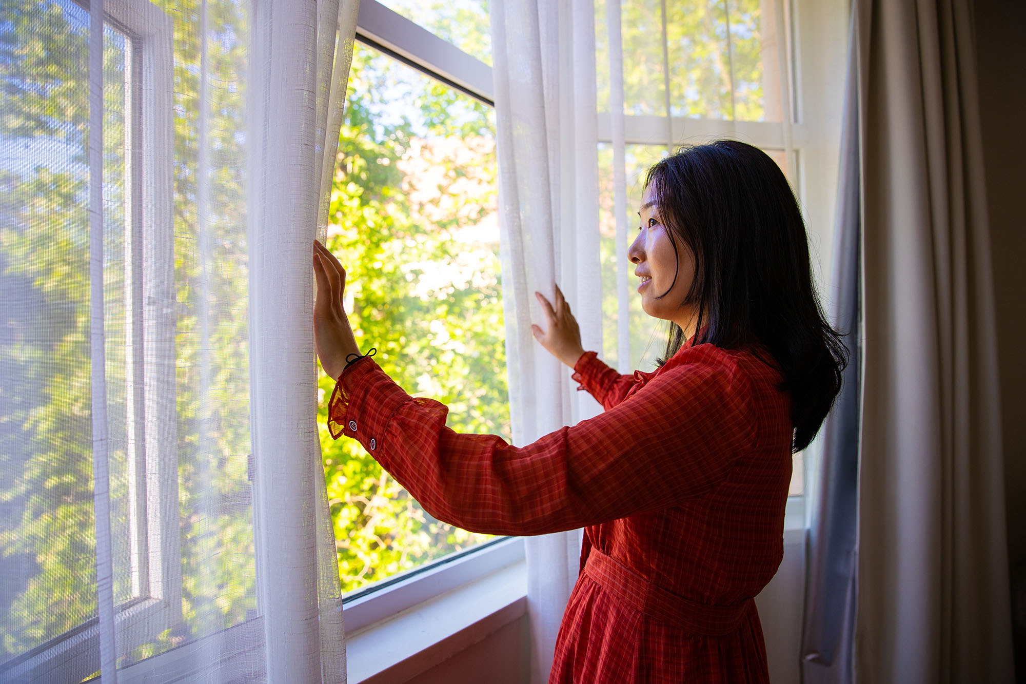 Woman in a home opening curtains and looking out the windows.