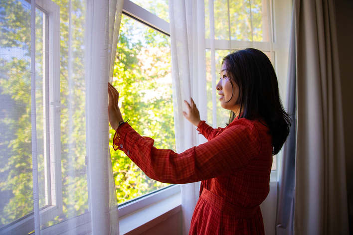 Woman in a home opening curtains and looking out the windows.