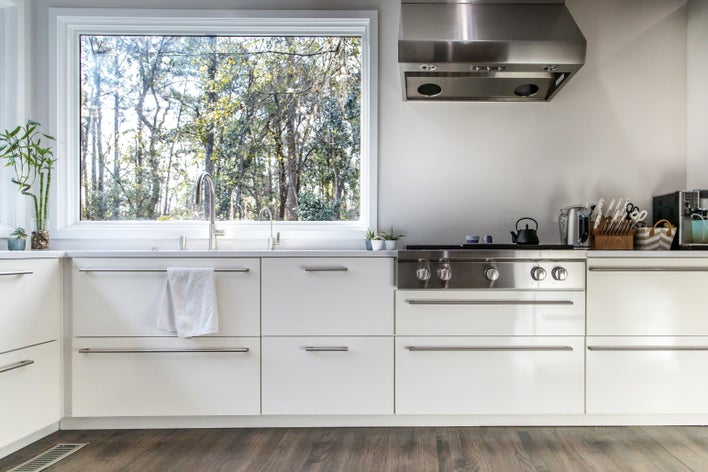 A large picture window above the kitchen sink in an all-white kitchen