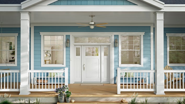 A light blue house with a large front porch featuring a white front door centered below a ceiling fan