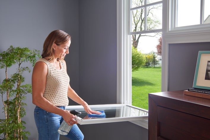 A woman cleaning the lower sash of a window that wouldn’t stay up before replacing it to test if it is fixed.