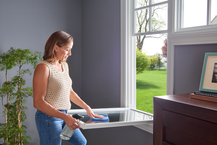 A woman cleaning the lower sash of a window that wouldn’t stay up before replacing it to test if it is fixed.